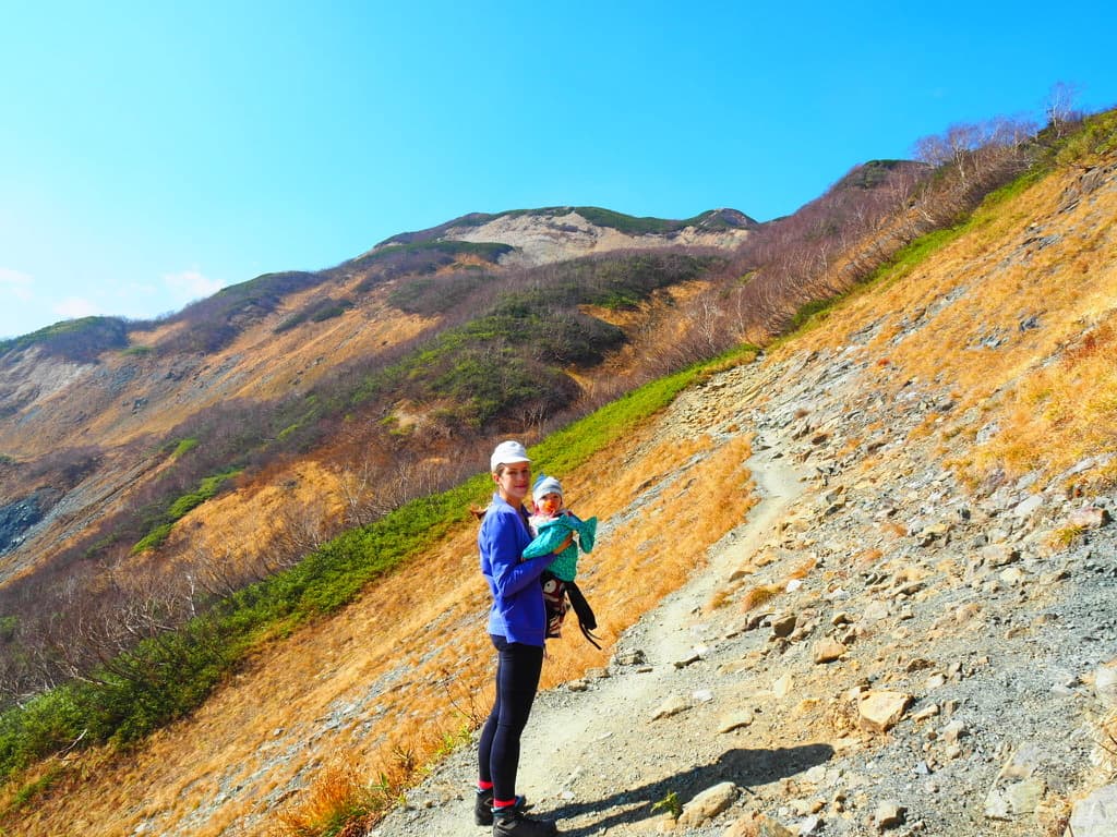 Natasha hiking a mountain trail with her baby in a carrier