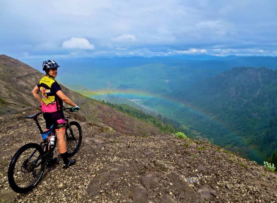 Mountain biking on a ridge with a rainbow over the valley